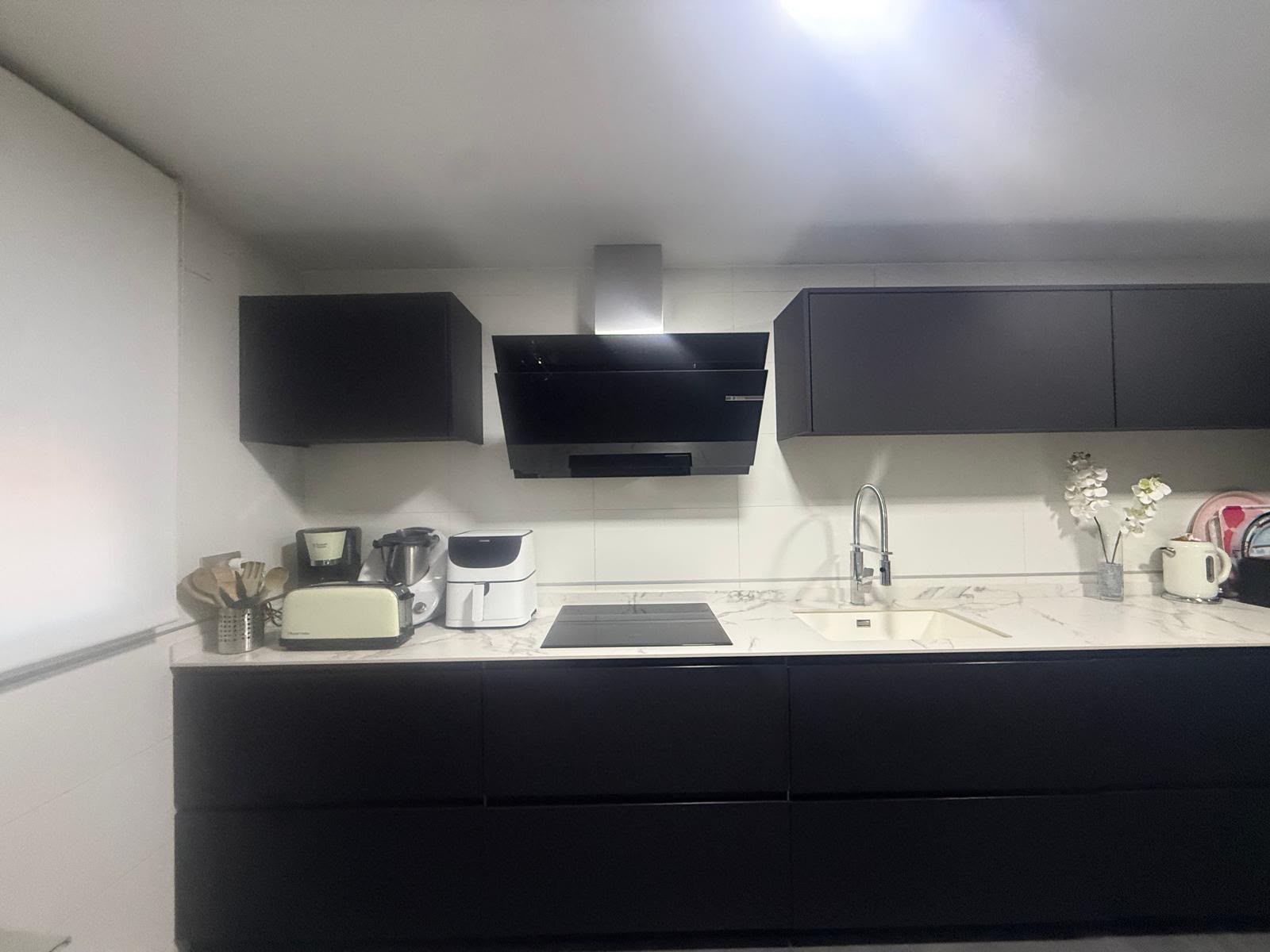 Cocina reformada con mobiliario negro y encimera de mármol